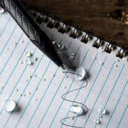 black pen writing on rite in the rain's weatherproof lined notebook. waterdroplets on notebook
