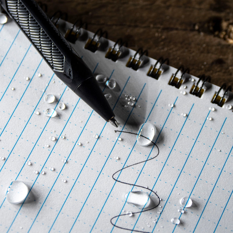 black pen writing on rite in the rain's weatherproof lined notebook. waterdroplets on notebook