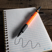 Orange mechanical pencil writing squiggly line on rite in the rain lined notebook paper with a wooden surface background
