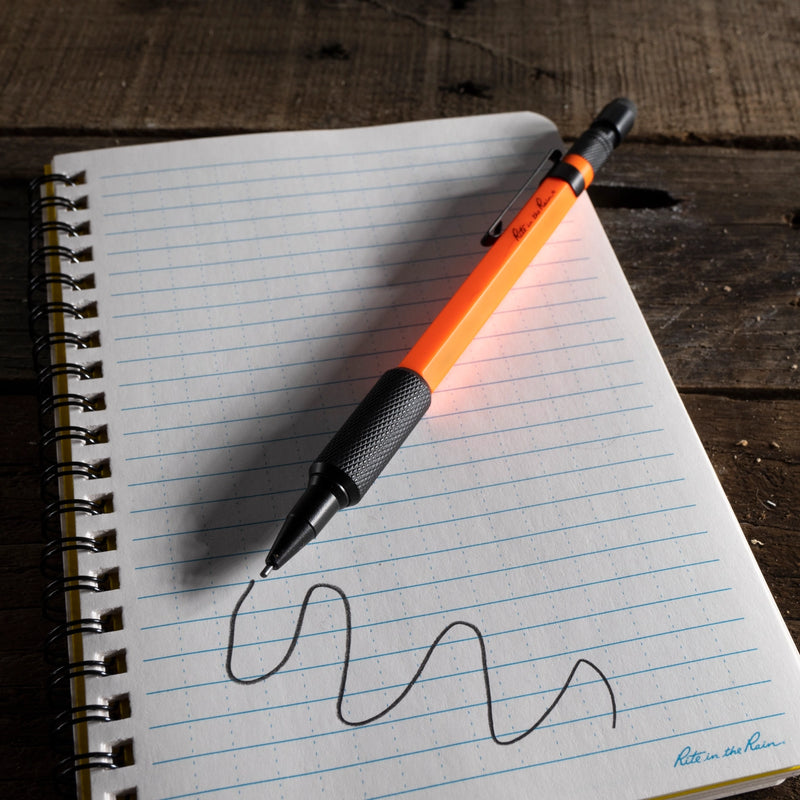 Orange mechanical pencil writing squiggly line on rite in the rain lined notebook paper with a wooden surface background