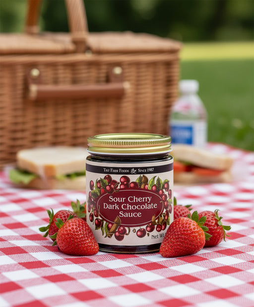 Jar of Sour Cherry Dark Chocolate Sauce with a gold lid on picnic blanket