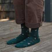adult person wearing dark green socks with woodpeckers and berries on a wood floor