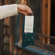 person holding up the green sock with woodpeckers and berries from twine hanger with label on