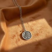 Silver necklace with a fern foliage pendant on a white background