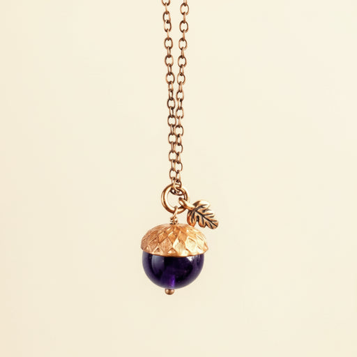 Necklace with acorn pendant and leaf charm on a neutral background