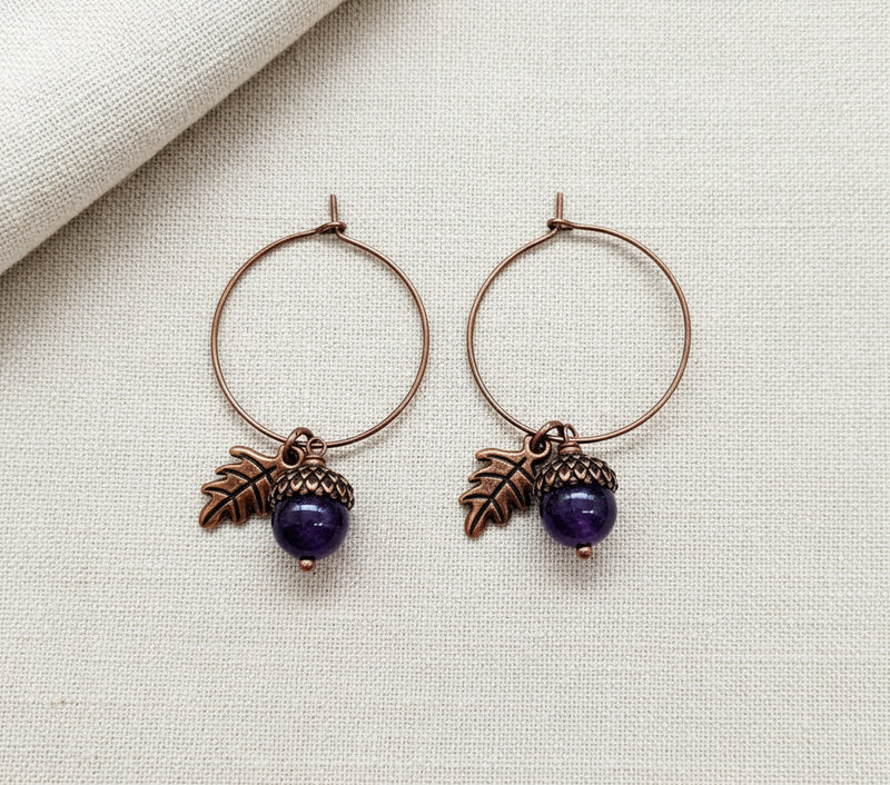 Pair of hoop earrings with leaf and purple arcorn charms on a white background