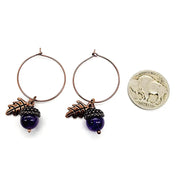 Pair of hoop earrings with purple acorns and leaf charms, next to a quarter for scale.
