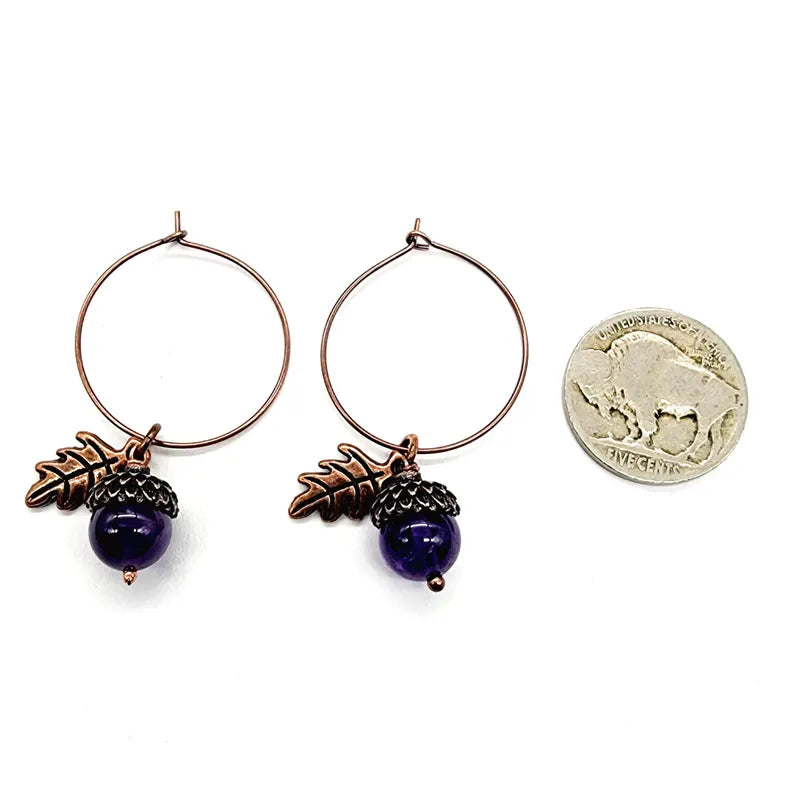 Pair of hoop earrings with purple acorns and leaf charms, next to a quarter for scale.