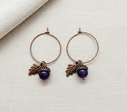 Pair of hoop earrings with leaf and purple arcorn charms on a white background