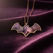 Bat-shaped necklace with a purple and pink gradient on a plum velvet background