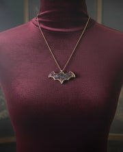 Mannequin wearing a purple turtleneck with a bat-shaped pendant necklace against a dark background
