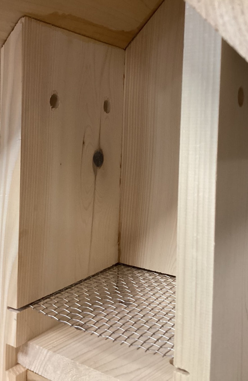 Close-up of a wooden birdhouse with a metal nest lift platform and side panel ventilation holes. 