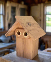 Wooden double-portal bluebird nest box with a rustic design on a wooden surface.