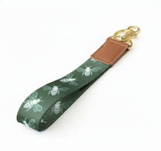 Keychain with bee pattern on a light green strap with gold ring and leather tab.