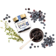 Jar of Blake Hill Wild Blueberry jam with fresh jam and a spoon on a white background