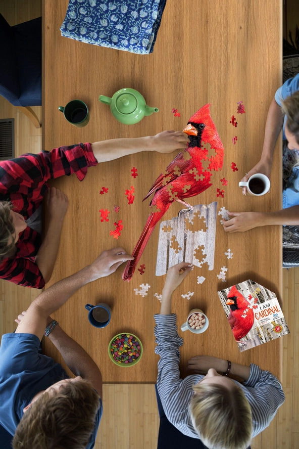 Family working on a puzzle of a cardinal at a dining room table, overhead view