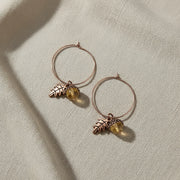 Pair of hoop earrings with leaf and acorn charms on a linen background