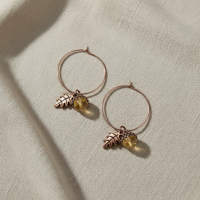 Pair of hoop earrings with leaf and acorn charms on a linen background