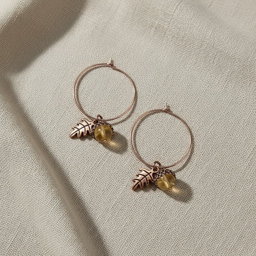 Pair of hoop earrings with leaf and acorn charms on a linen background