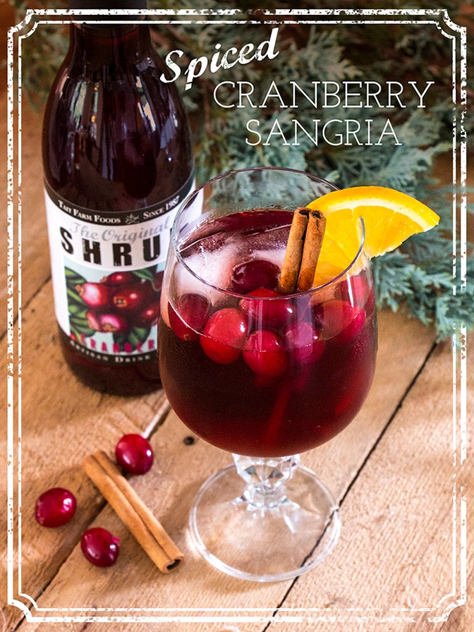 Spiced cranberry sangria with a bottle of Shrub on a wooden surface.