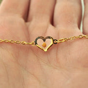 Gold necklace with a heart-shaped charm and mustard seed held in a hand