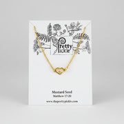 Gold necklace with heart pendant enclosing a mustard seed