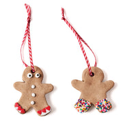 two homemade gingerbread man ornaments decorated and string with white and red striped string