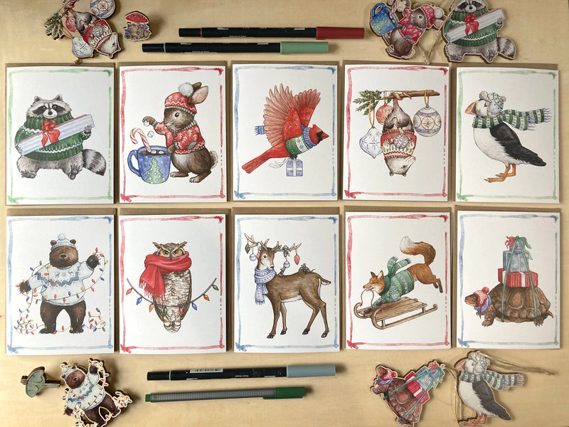 Set of greeting cards with animal illustrations wearing winter clothing on a wooden surface.