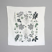 A white kitchen towel with green and black foliage and firefly designs.