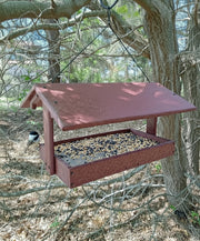 Cherrywood bird feeder hanging from a tree with a chickadee perched on it