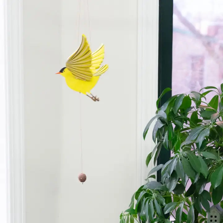 Yellow bird-shaped mobile against a white wall with a plant in the foreground