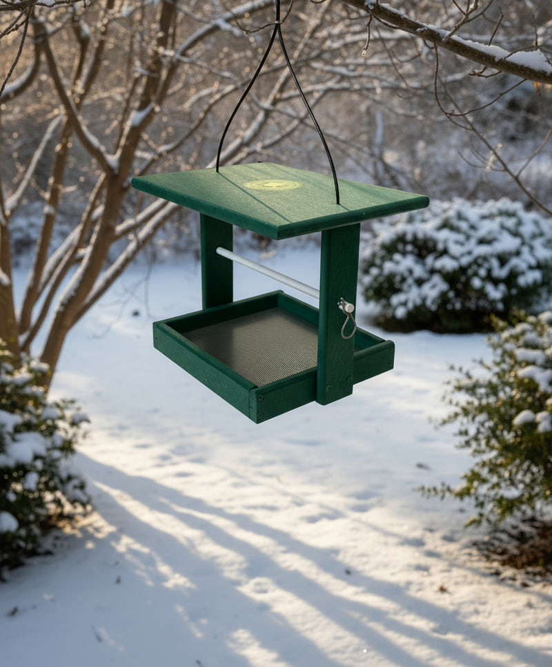 Green cylinder feeder with a tray on in a winter garden setting

