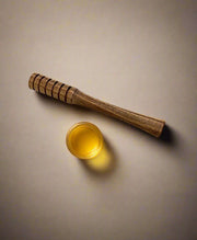 Wooden honey dipper and glass jar of honey on a beige background