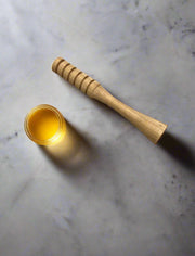 Wooden honey dipper and jar of honey on a marble surface