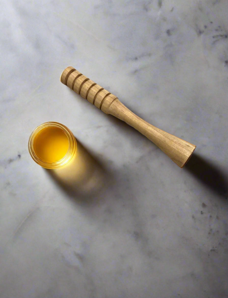 Wooden honey dipper and jar of honey on a marble surface