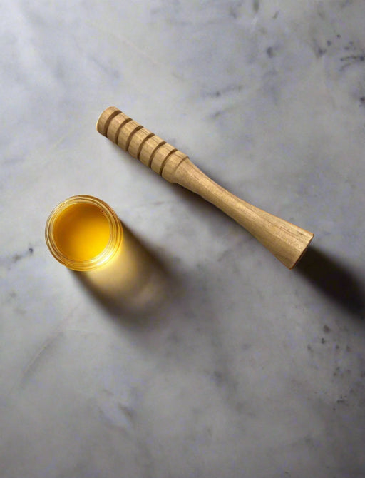 Wooden honey dipper and jar of honey on a marble surface