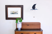 blue kingfisher mobile pull string next to a framed picture on a wall.