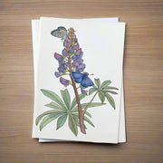 Note card with a floral design featuring lupin flowers and Karner's butterflies on a natural wood background