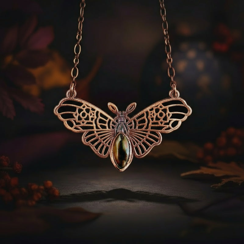 Copper witch moth necklace with a central gemstone on a dark background