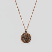 Bronze textured back of pendant on a chain against a white background