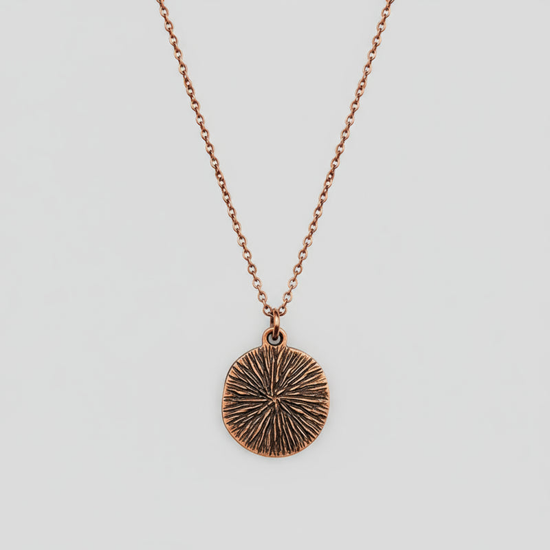 Bronze textured back of pendant on a chain against a white background