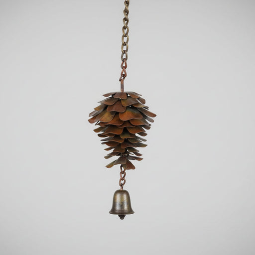 Decorative pine cone with a bell hanging on a chain against a plain background