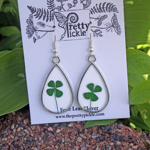 Teardrop-shaped earrings with four-leaf clover design on a 'Pretty Pickle' branded card, set against a natural background.