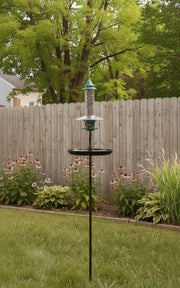 Bird feeder on a stand in a garden with autumn trees and flowers.