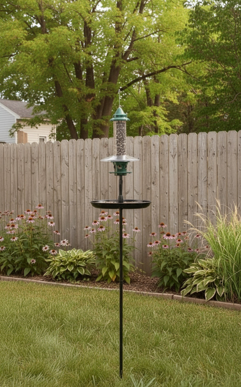 Bird feeder on a stand in a garden with autumn trees and flowers.