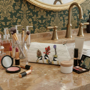 Cosmetic bag featuring three chickadees in botanical headwear: a pinecone, cardinal flower, and blazing star all on a pale cream wood slat background 