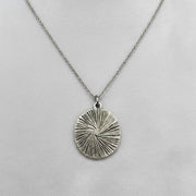 Silver necklace with a textured circular pendant on a white background