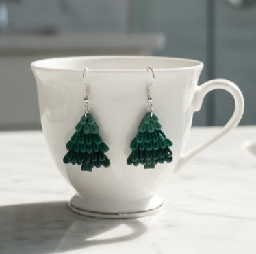 Holiday tree earrings displayed on a white China cup with a neutral background