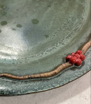 Closeup of ceramic plater with a branch and red berries on a light background