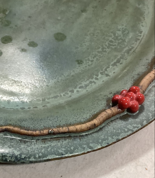 Closeup of ceramic plater with a branch and red berries on a light background